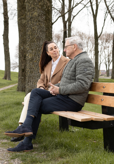 Coach verlies noord Fotografie van Coach Ingrid Jansen die met een oudere man praat tijdens een coachingssessie buiten op een bankje in Sloten, omringd door bomen en water